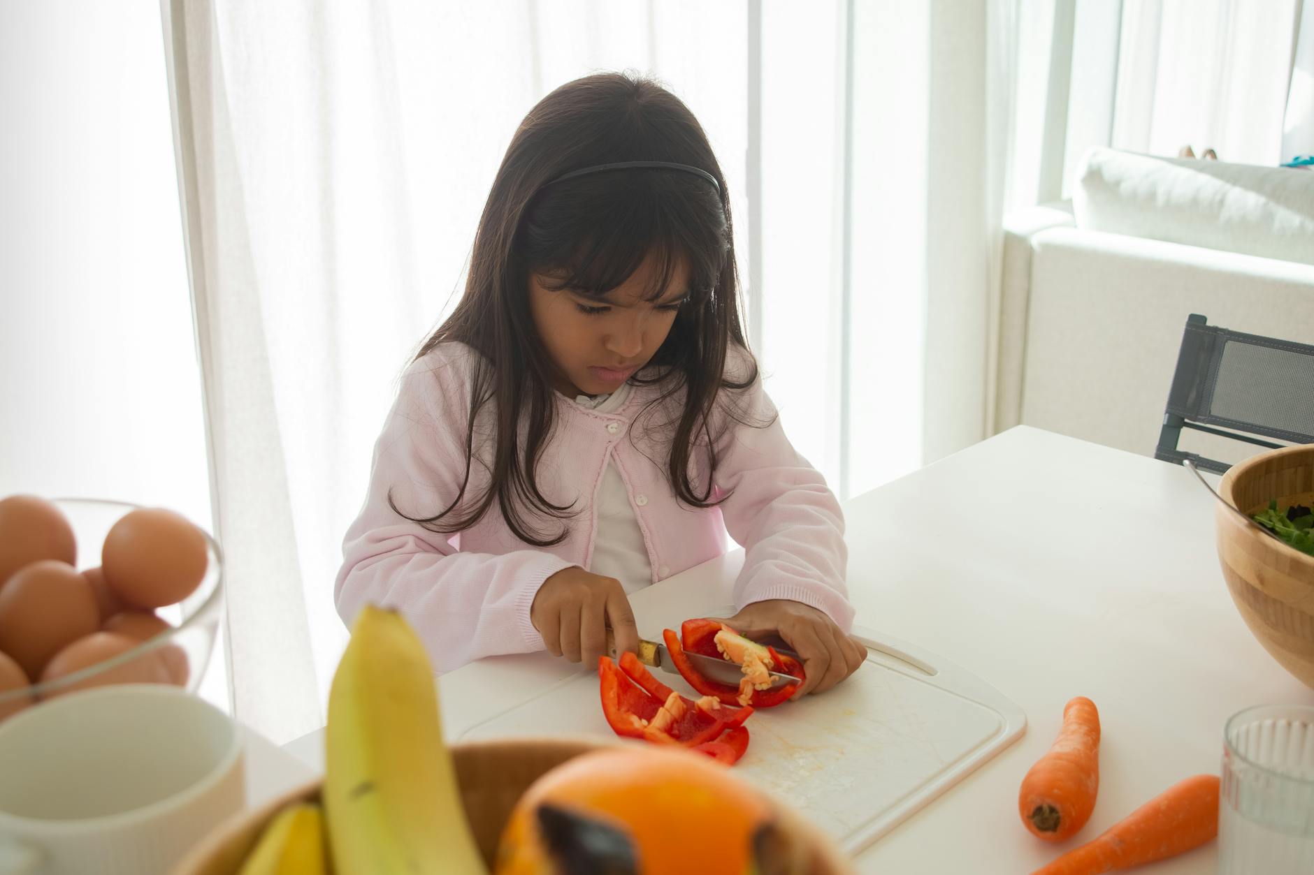 girl cutting red bell pepper using a knife